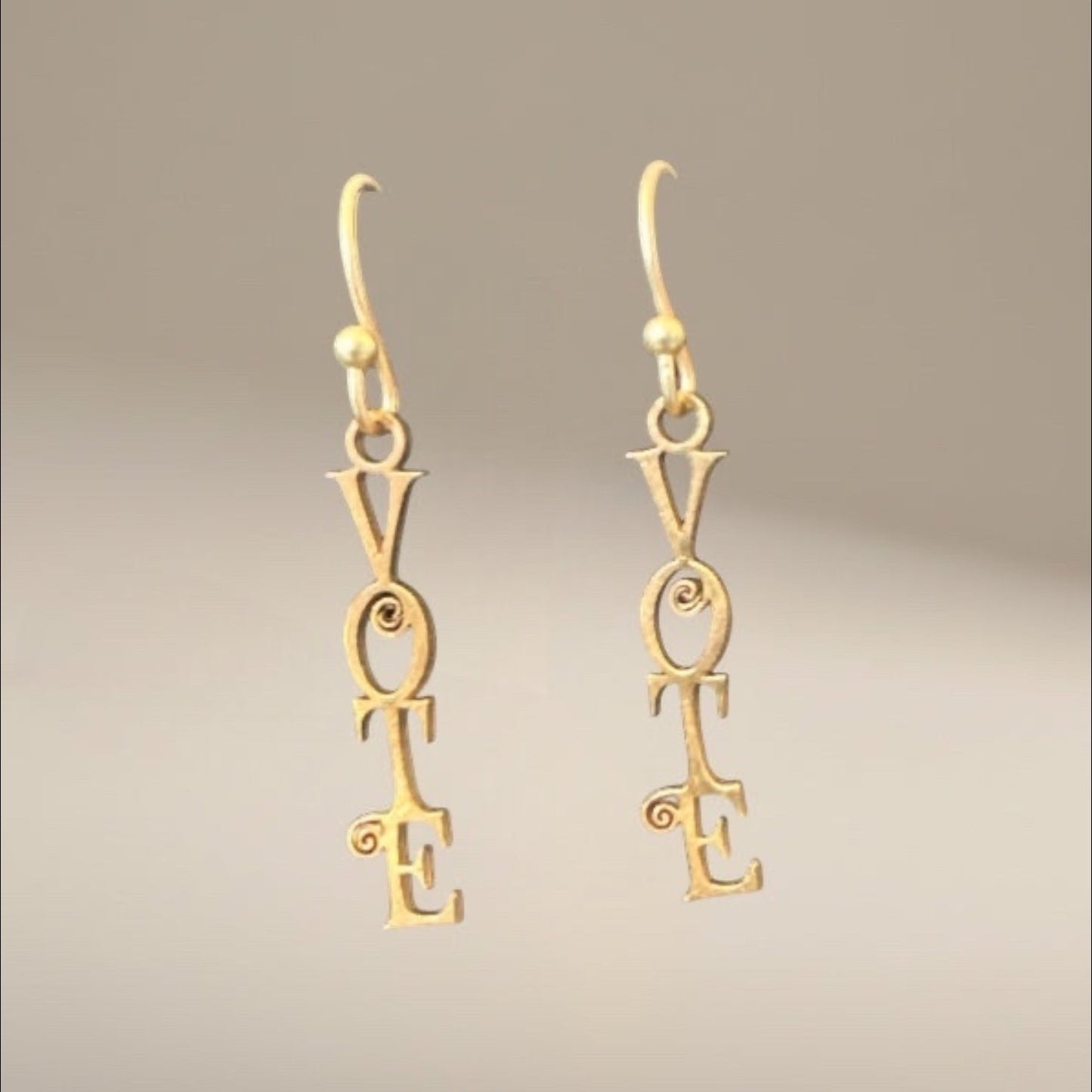 Bedrock Rose gold-tone dangle earrings with "VOTE" script and decorative scrolls. Laser-cut statement jewelry.