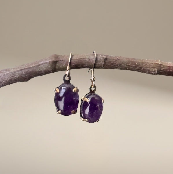 Bedrock Rose amethyst prong set oval earrings with gold-tone prongs hanging from a branch.