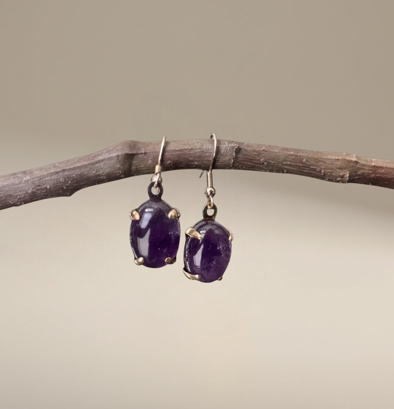 Bedrock Rose amethyst prong set dangle earrings with oval-cut purple stones and gold-tone prongs.