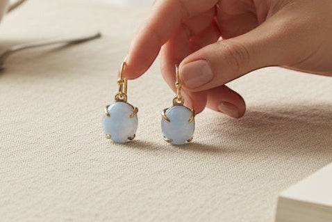 Person holding a pair of earrings on a table with a cup of tea and sunglasses.