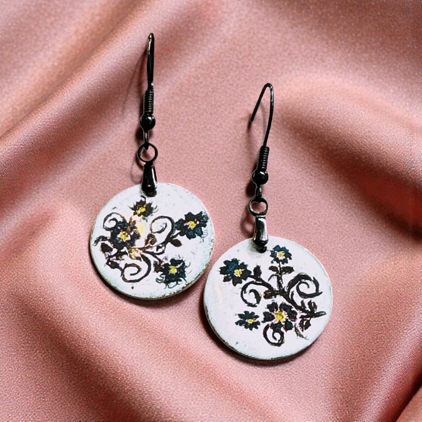 Pair of round earrings with floral designs on a pink fabric background