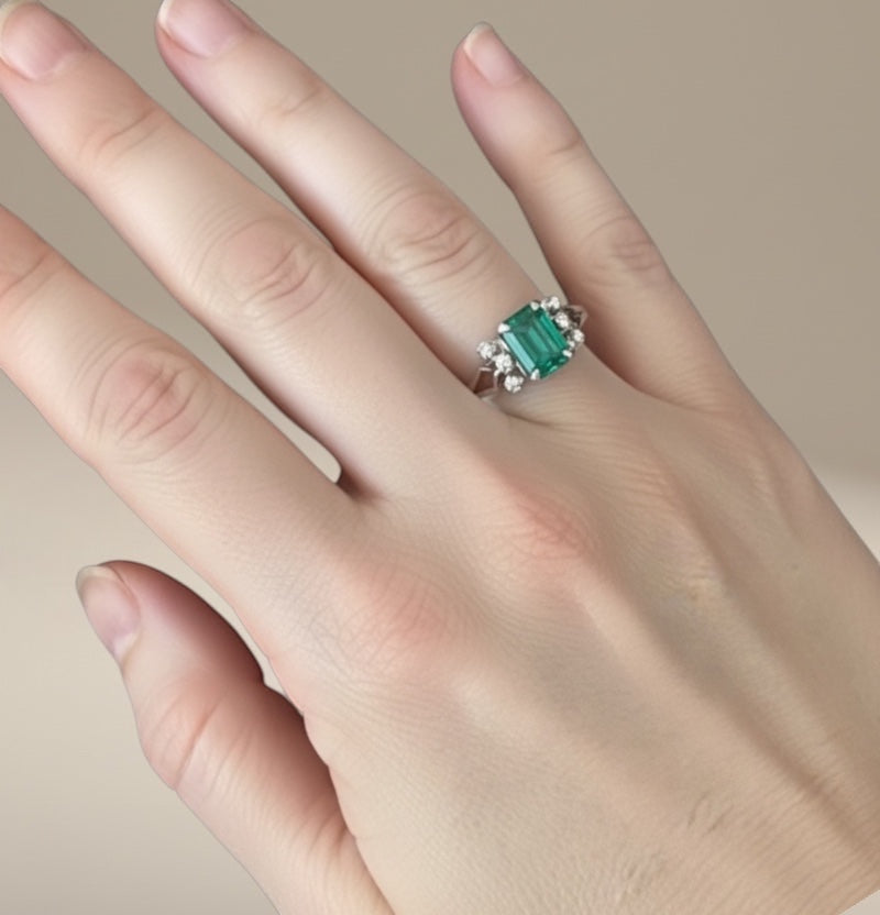Bedrock Rose emerald cut emerald ring with diamond accents on a silver band, worn on a finger.