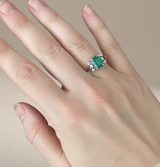 Bedrock Rose emerald cut emerald ring with diamond accents on a hand.