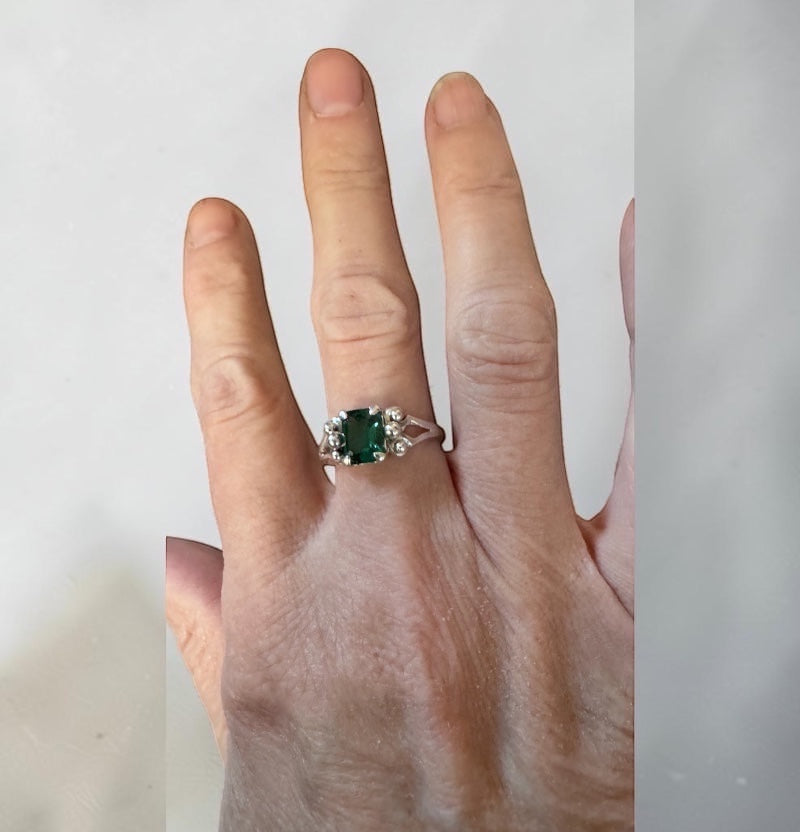 Bedrock Rose emerald cut emerald ring with diamond accents on a silver band.