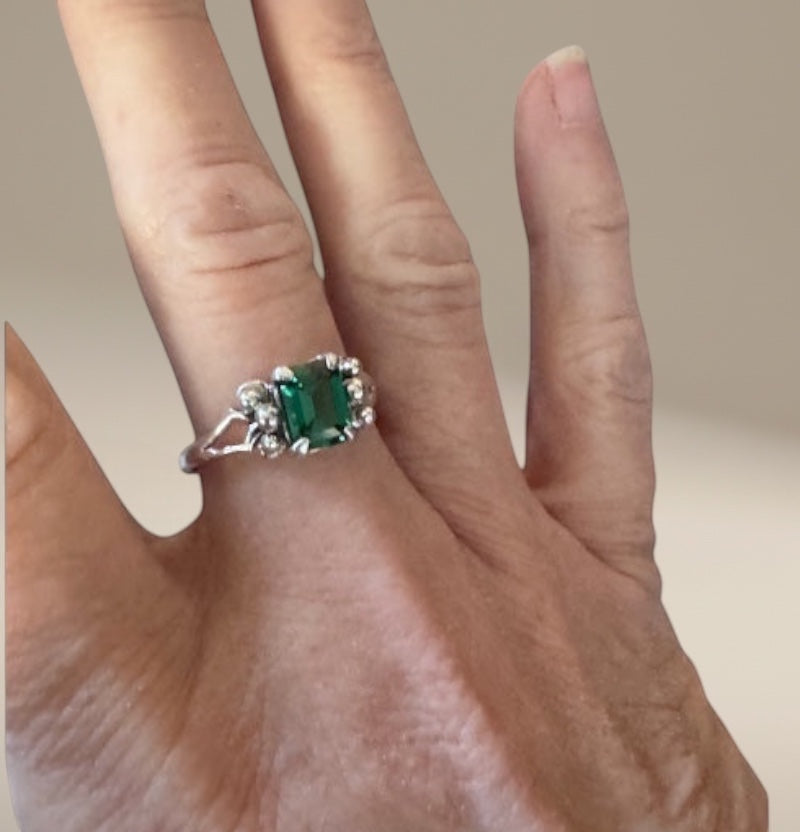 Bedrock Rose emerald cut emerald ring with diamond accents on a silver band.