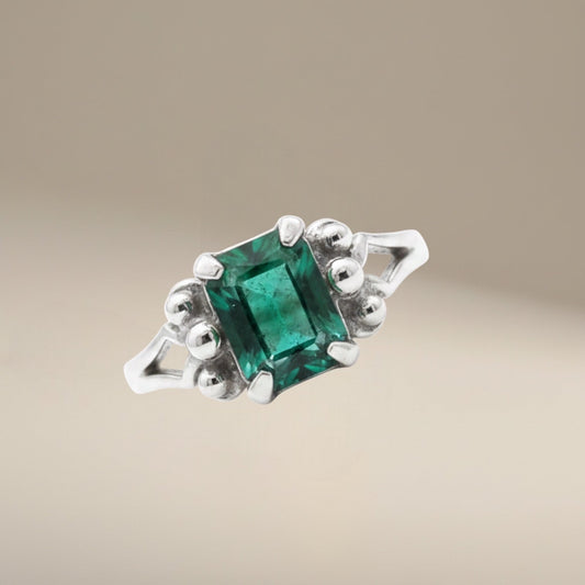Bedrock Rose emerald cut emerald ring with diamond accents on a silver band.