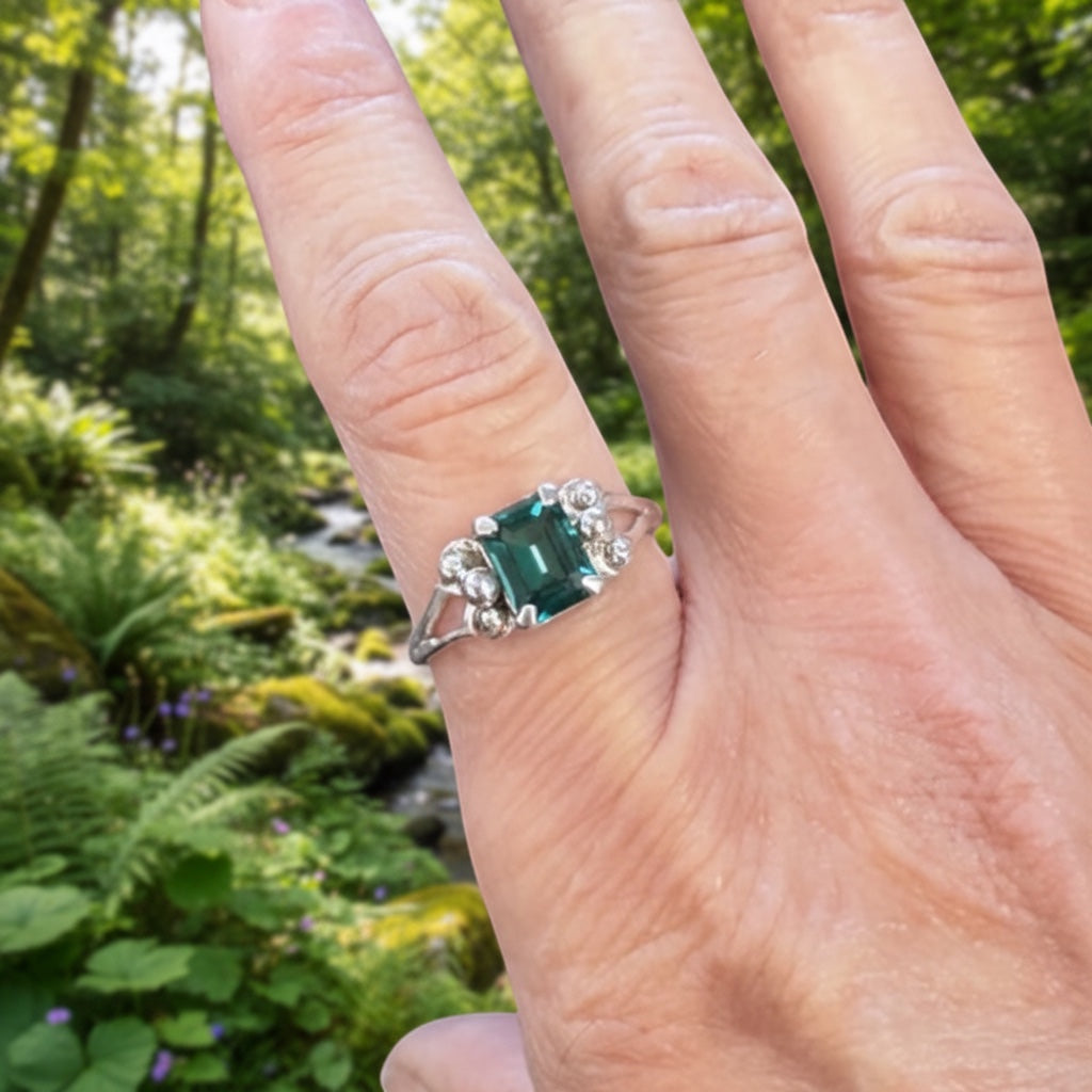 Bedrock Rose emerald cut emerald ring with diamond accents on a silver band.