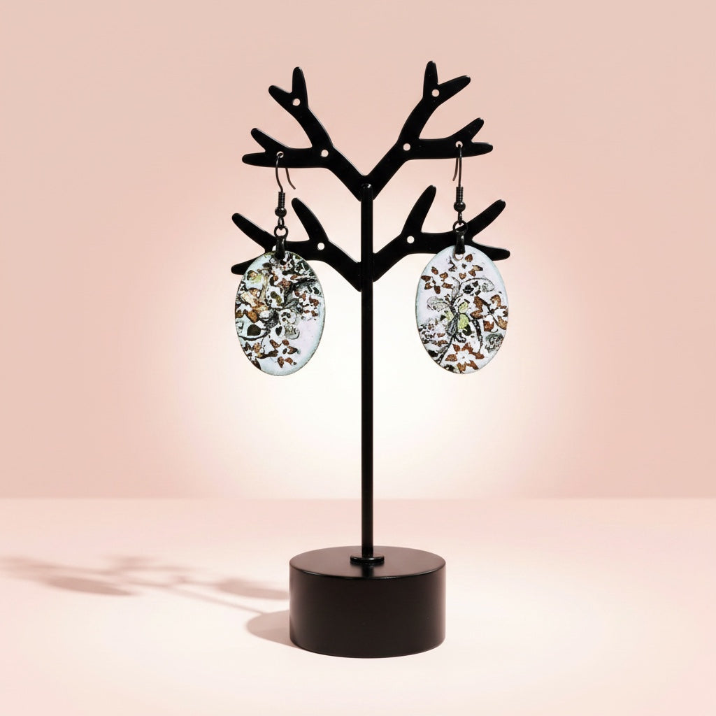 Bedrock Rose hand-enameled oval copper earrings with a white base and black floral botanical design. Dangle style.