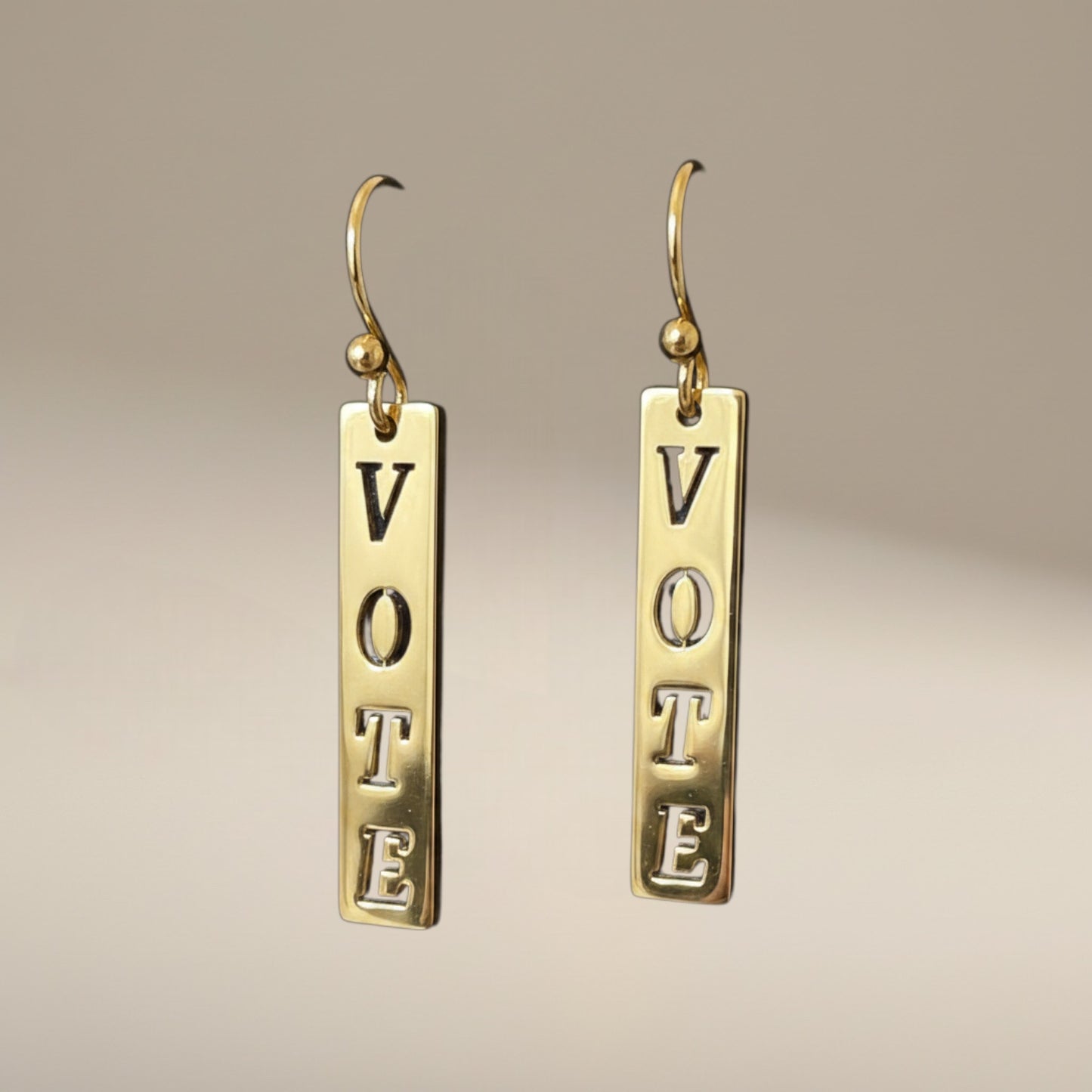 Bedrock Rose gold-plated dangling earrings with laser-cut "Vote" text. Dangling bar earrings with hook closure.