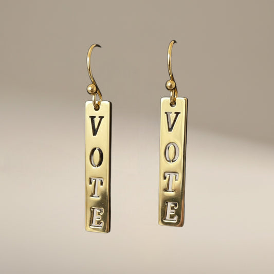 Bedrock Rose gold-plated dangling earrings with laser-cut "Vote" text. Dangling bar earrings with hook closure.