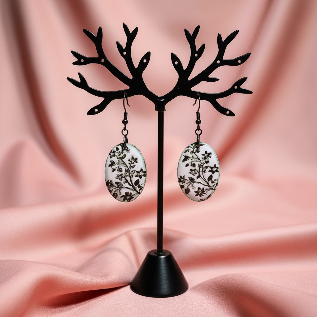 Bedrock Rose hand-enameled oval copper earrings with black floral motif on white base. Artisan jewelry.