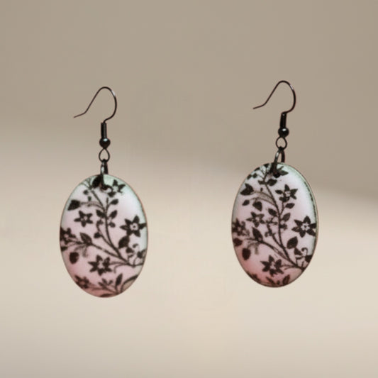 Bedrock Rose hand-enameled oval dangle earrings with black floral motif on white enamel, copper base.