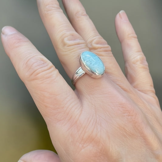 Bedrock Rose oval larimar ring with a silver band, set on a hand.