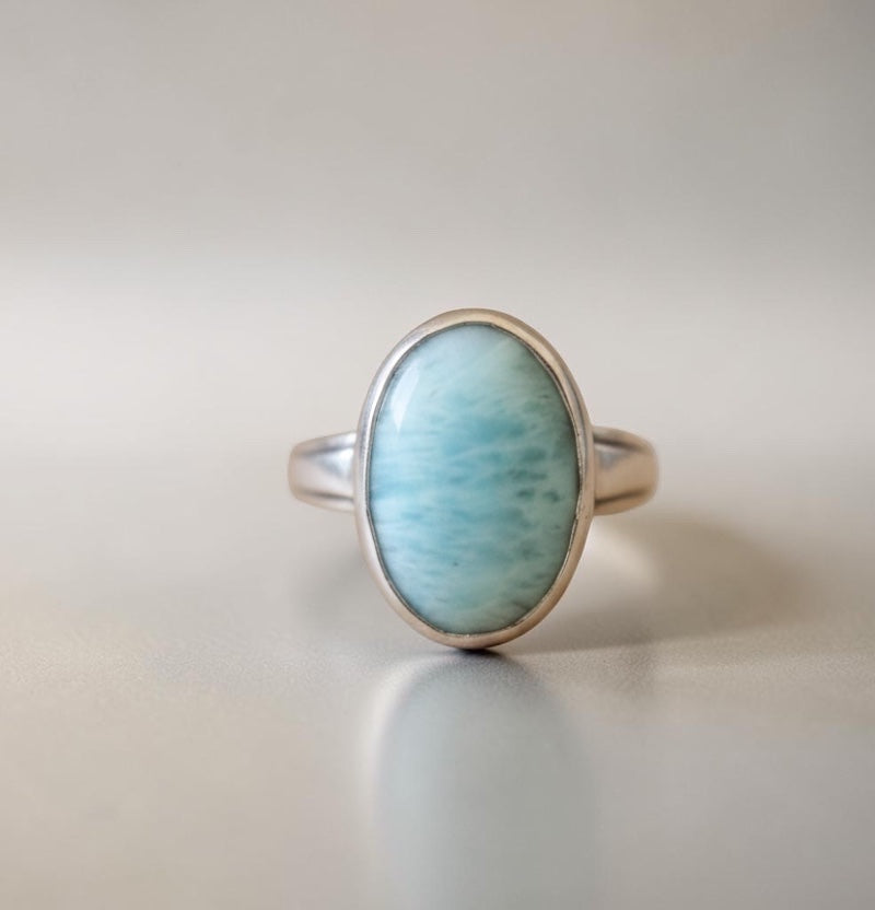Bedrock Rose oval larimar ring with a silver band. The stone is a pale blue with white marbling.