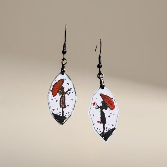 Bedrock Rose artisan shield earrings with hand-painted red umbrella and silhouette design on white enamel.