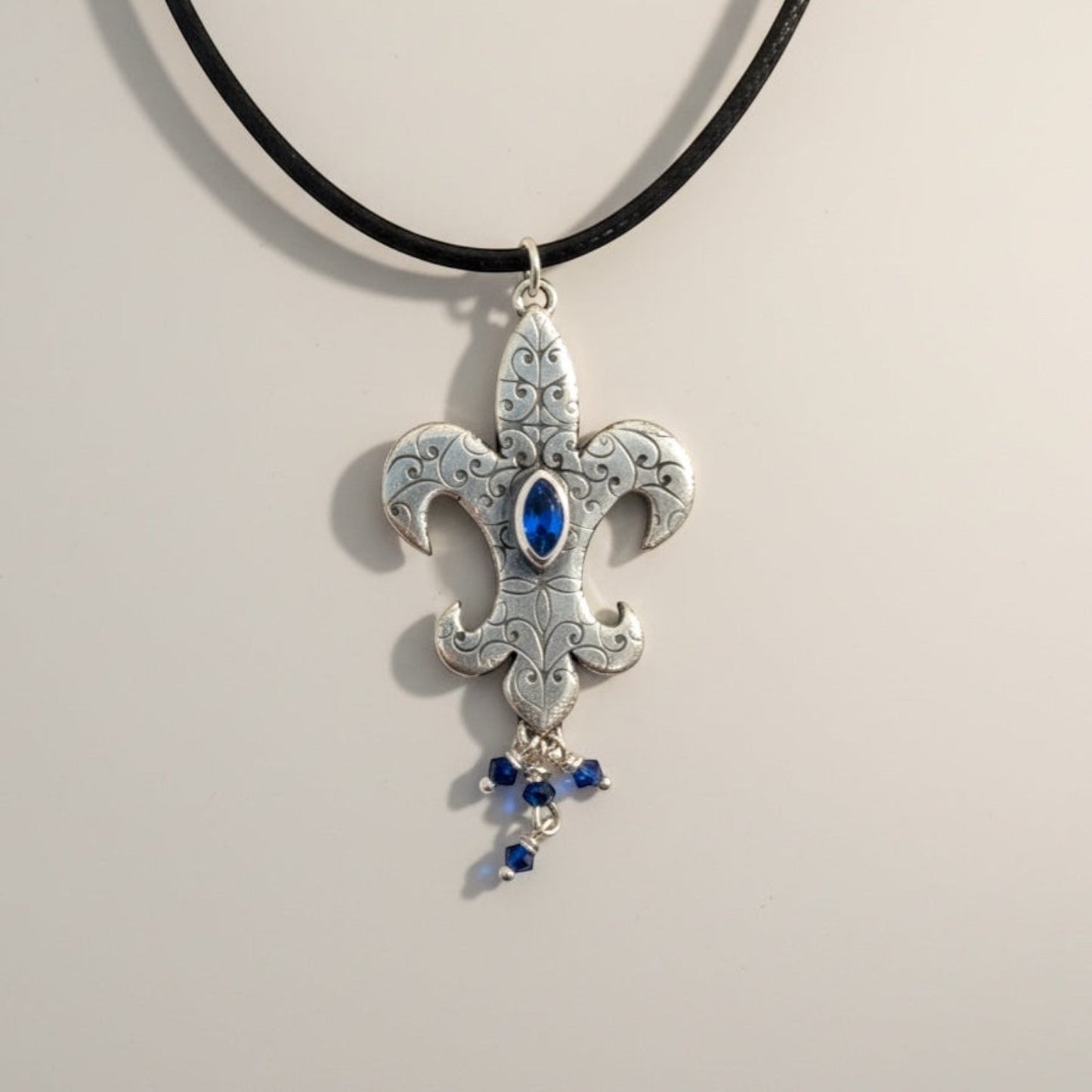 Bedrock Rose sterling silver fleur-de-lis pendant with blue marquis gemstone and dangling blue crystals.