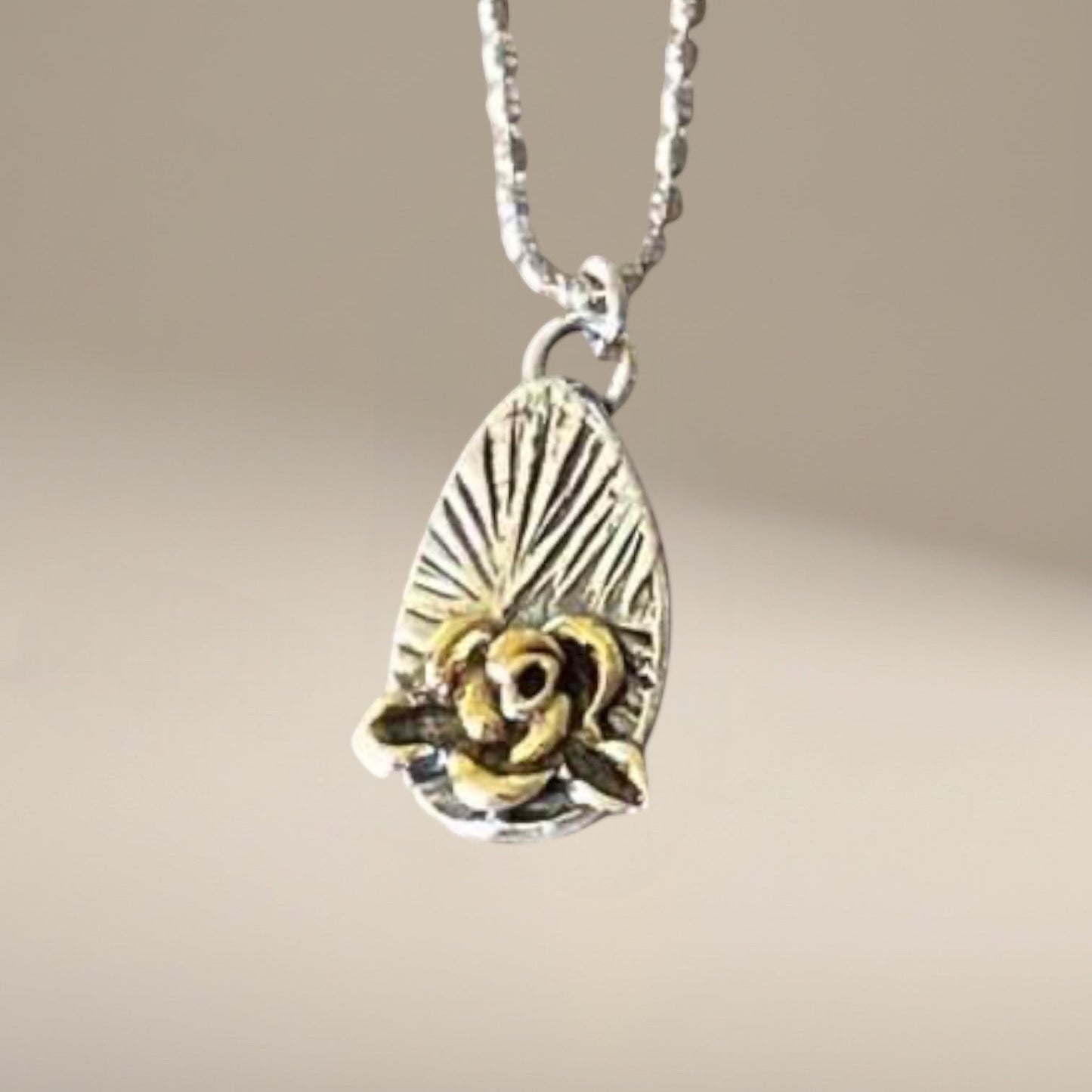 Bedrock Rose silver and gold rose pendant on a faceted ball chain necklace. Rose detail with sunburst background.