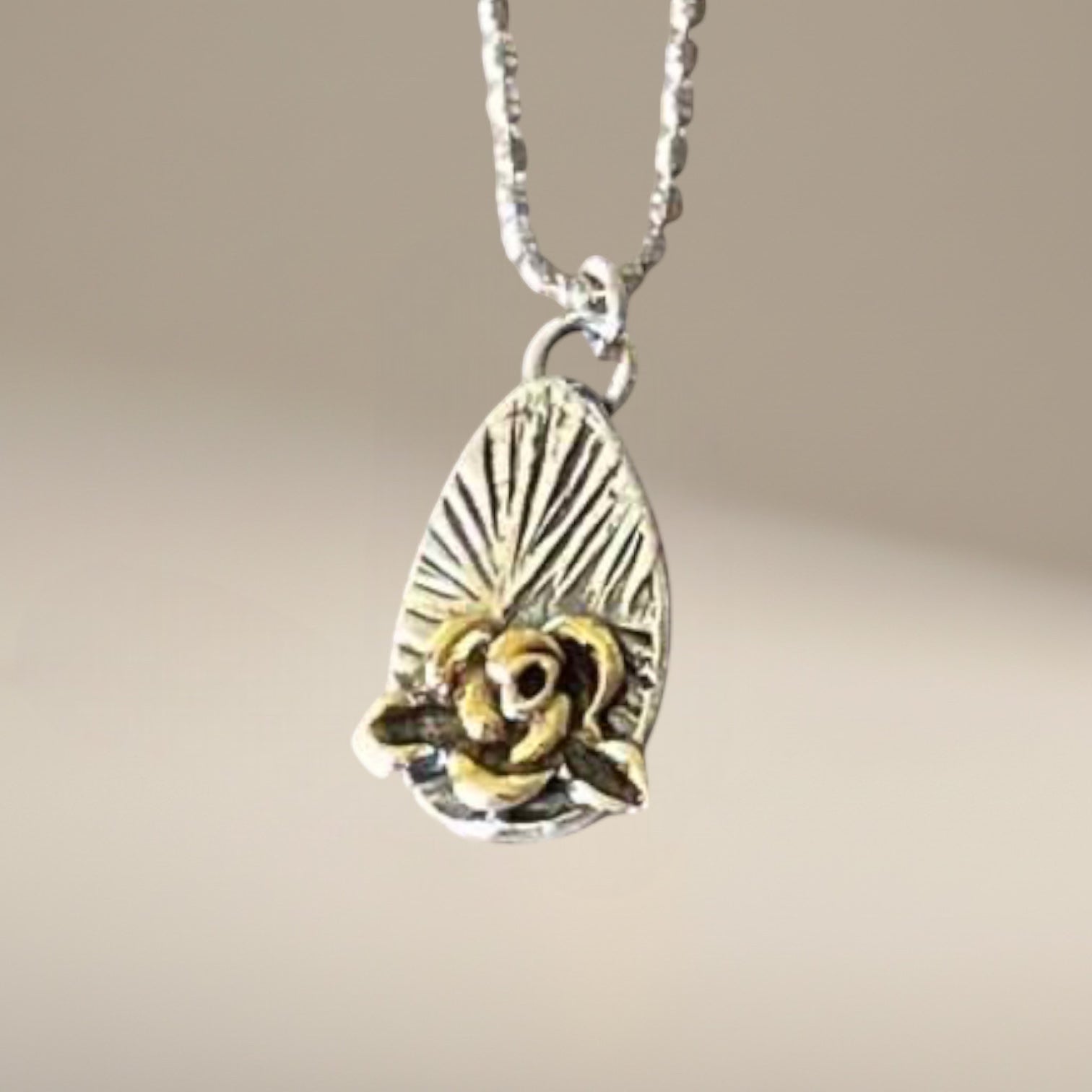 Bedrock Rose silver and gold rose pendant on a faceted ball chain necklace. Rose detail with sunburst background.
