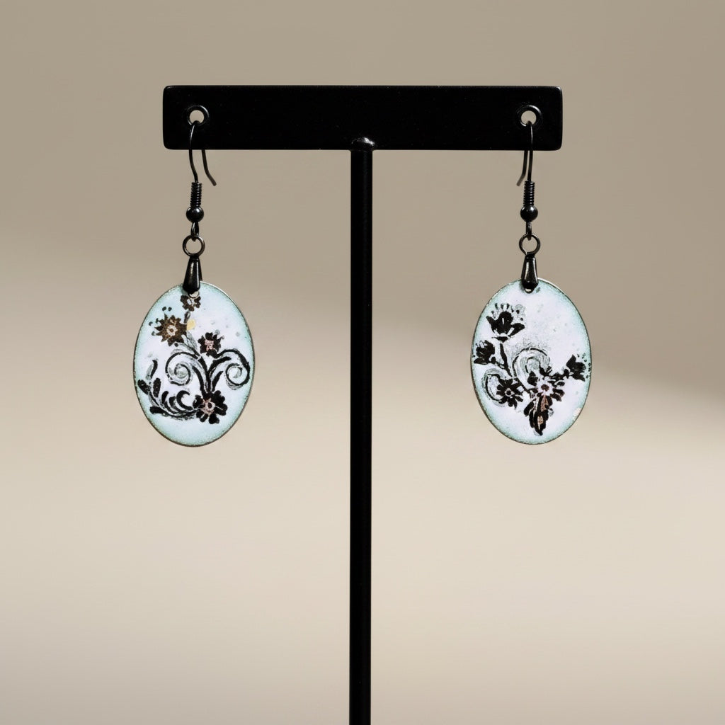 Bedrock Rose petite oval enameled dangles with black floral scroll design on white background.