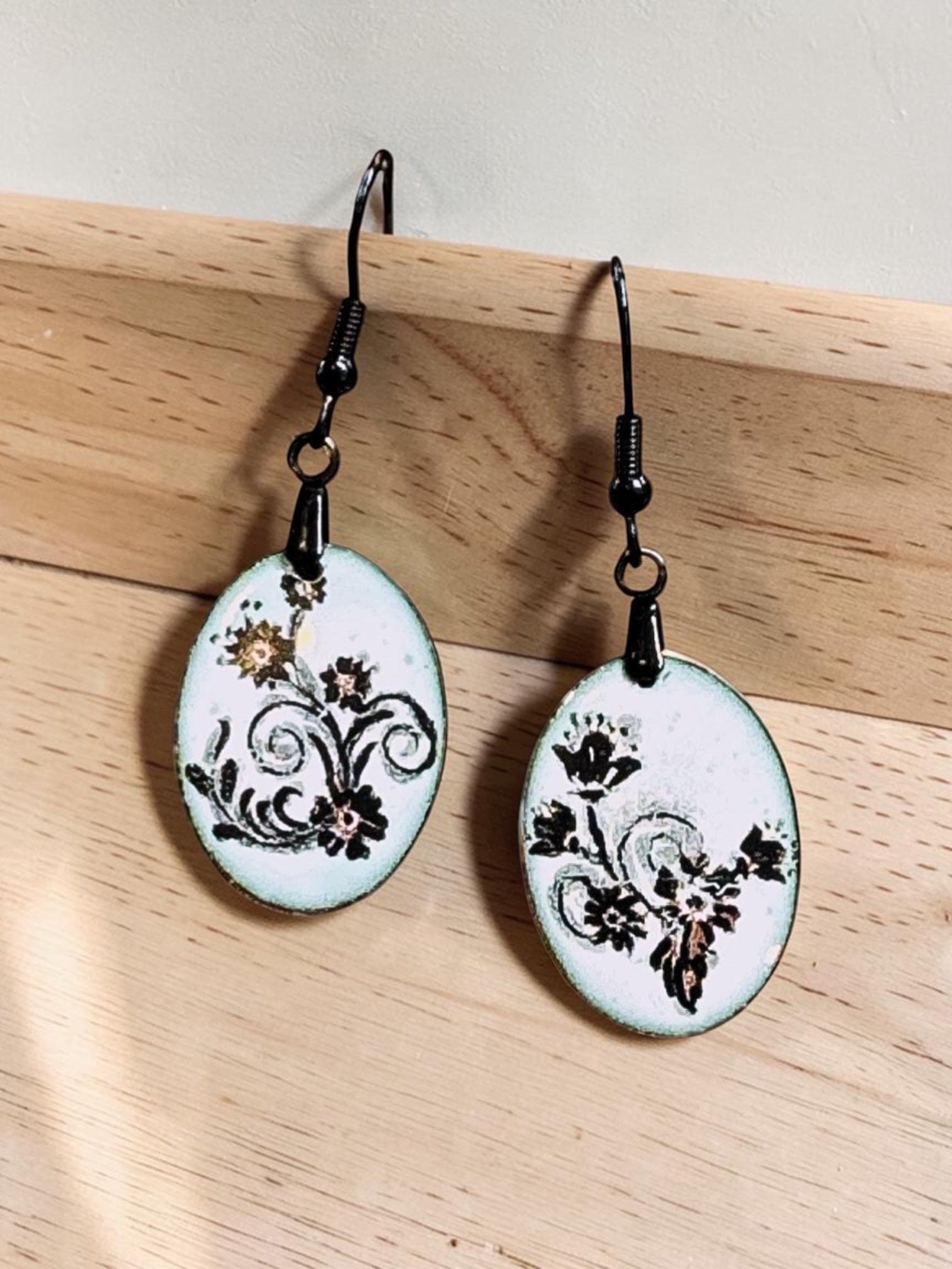 Bedrock Rose petite oval enameled dangle earrings with black floral scroll design on white.