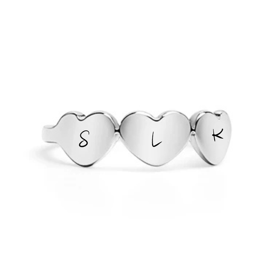Three heart-shaped silver charms with engraved letters on a white background