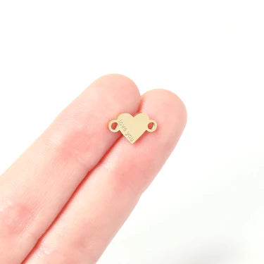 Gold heart-shaped jewelry piece on a finger against a white background